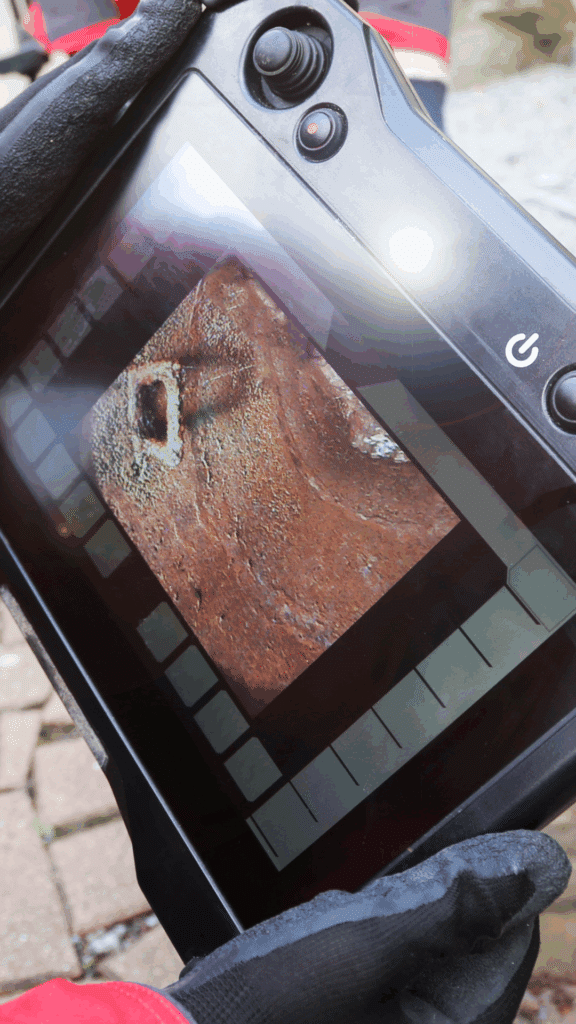 Close-up of a plumber's sewer camera inspection monitor showing a broken or corroded pipe interior.