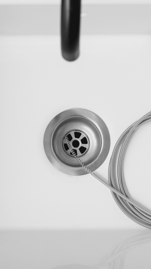 Close-up of a chrome bathroom sink drain and stopper, with a metal drain snake cable resting nearby, representing drain cleaning in Glendale, AZ.