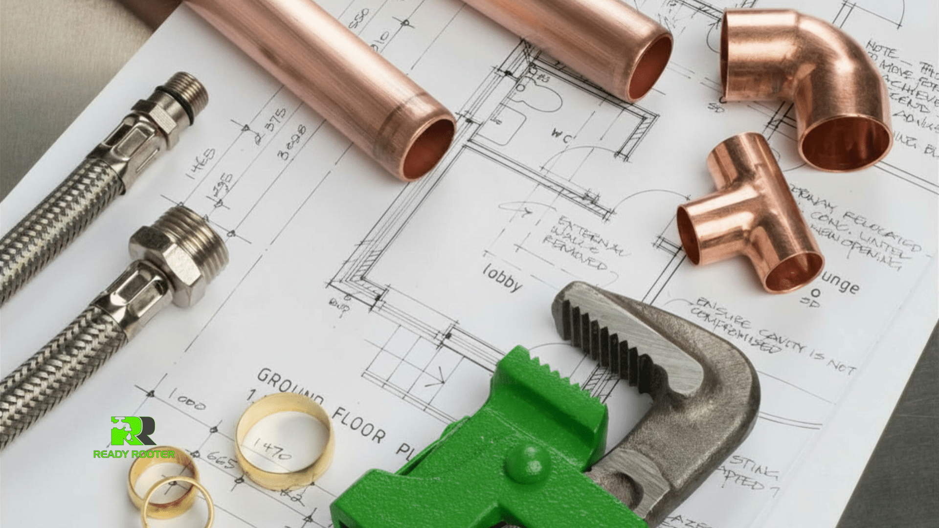 Copper pipe fittings and a pipe wrench resting on plumbing blueprints